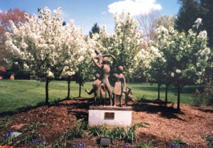 sculpture of a family in front of flowering trees